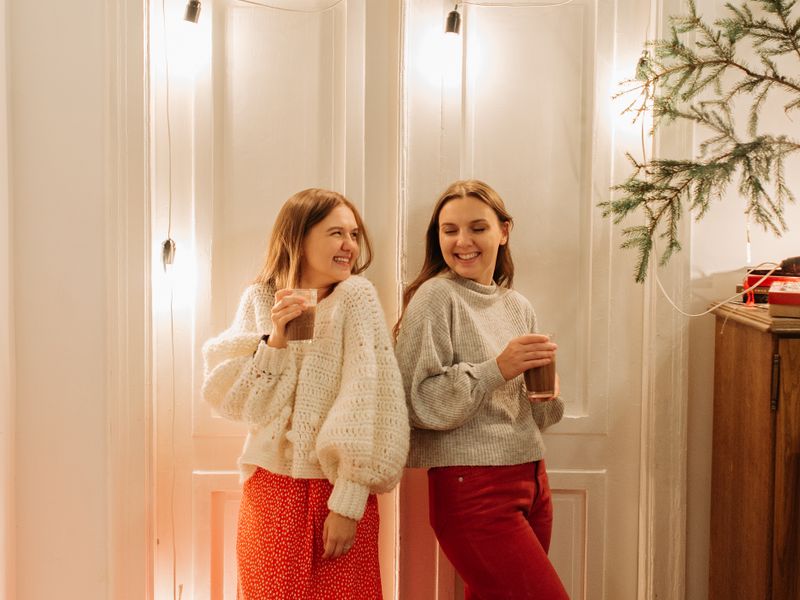 Two women in cozy holiday sweaters with warm drinks